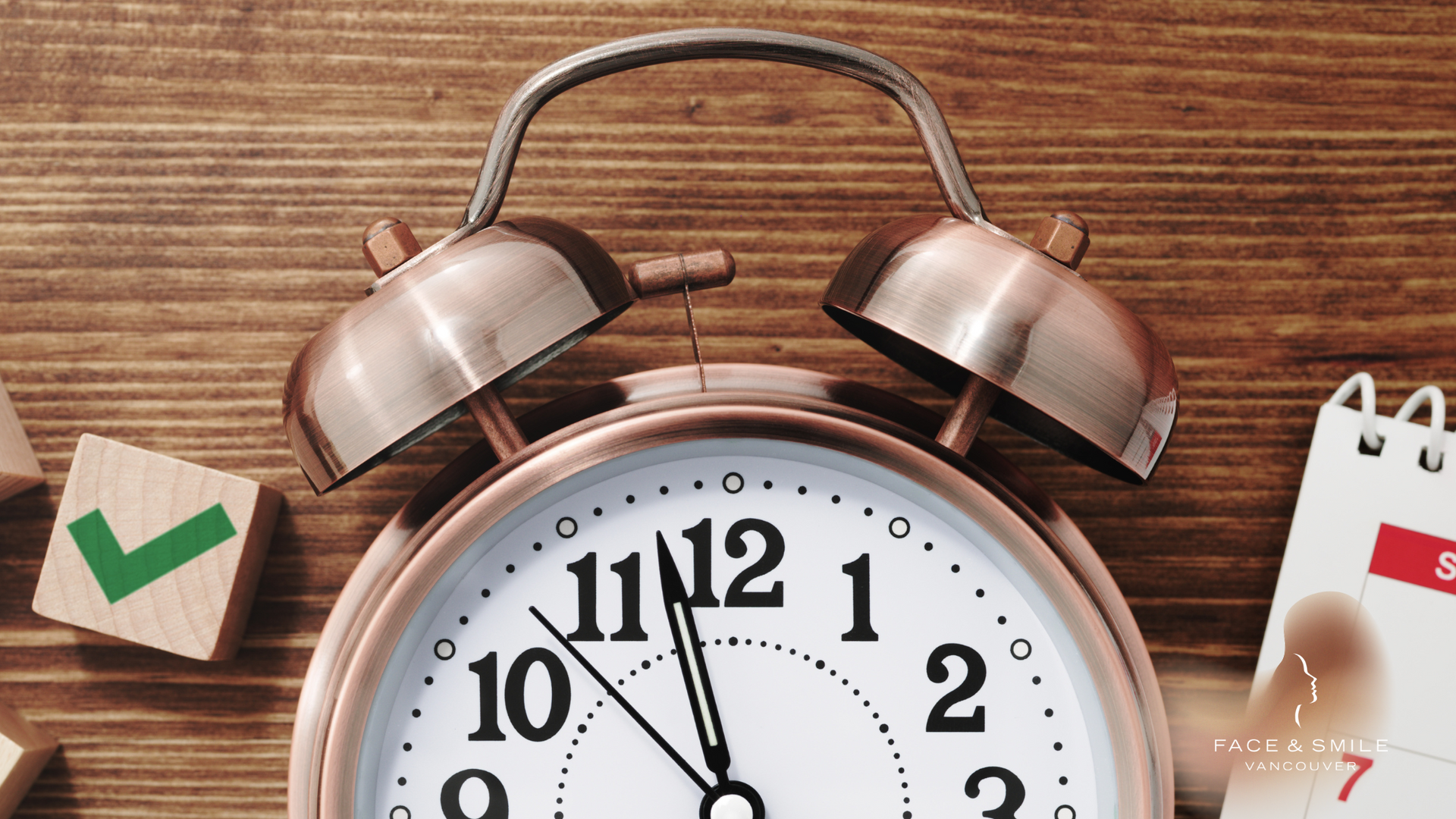 Close-up of a silver alarm clock beside a green check mark and a calendar page on a wooden table