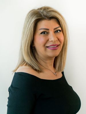 A woman wearing a black off the shoulder top and a necklace is smiling for the camera.