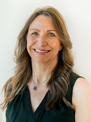 A woman wearing a black shirt and a necklace is smiling for the camera.