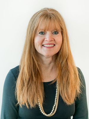 A woman with long red hair and a pearl necklace is smiling for the camera.
