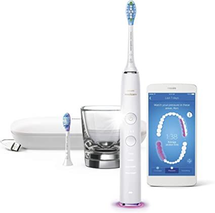 A white electric toothbrush with a smart phone next to it.