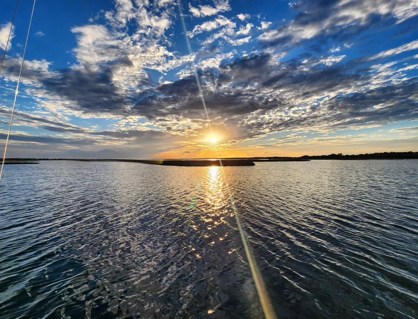 Sunset over water with sun reflecting, blue sky with clouds.