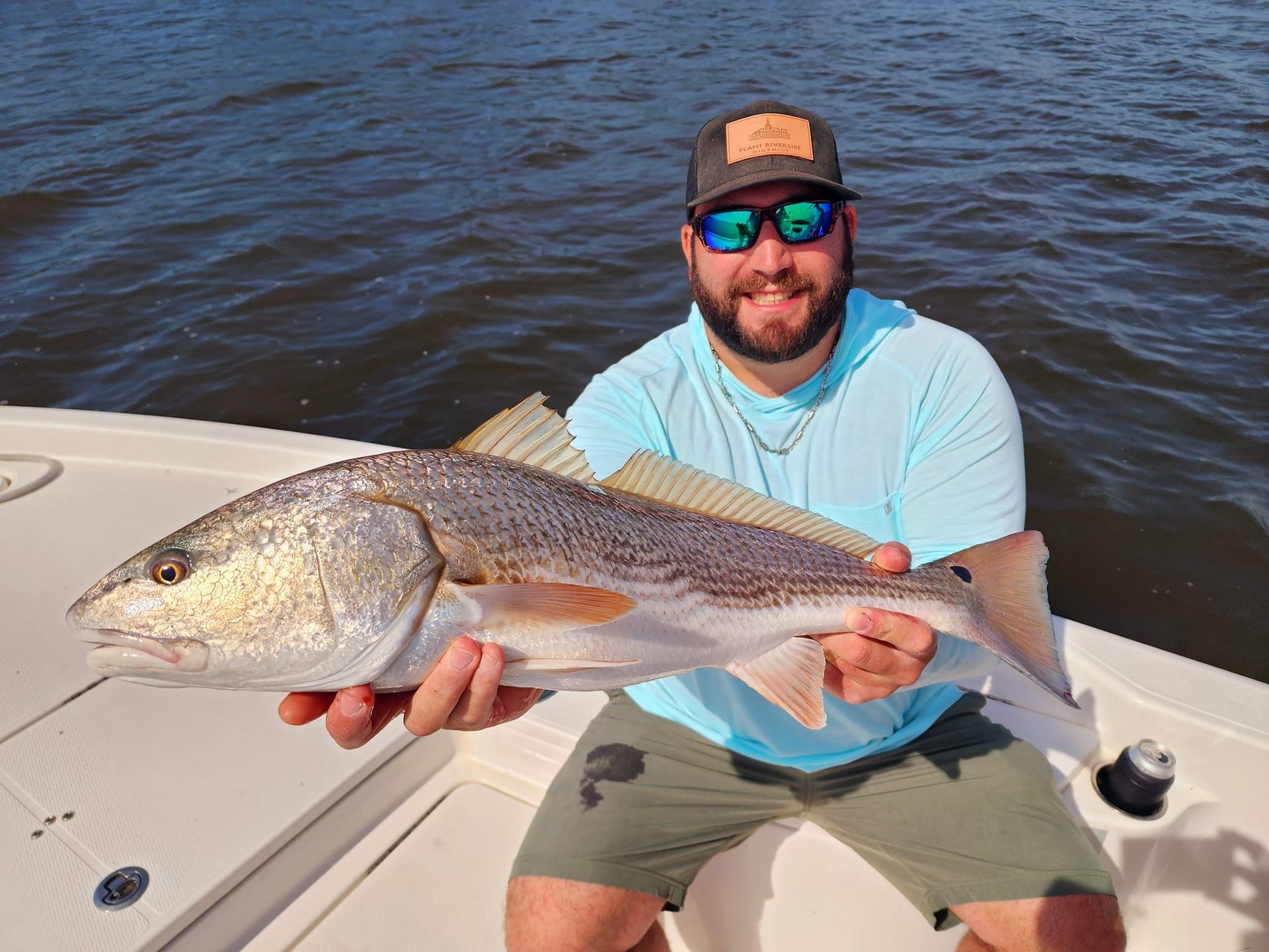 Man holding a redfish on a boat, smiling. The water and sky are in the background.