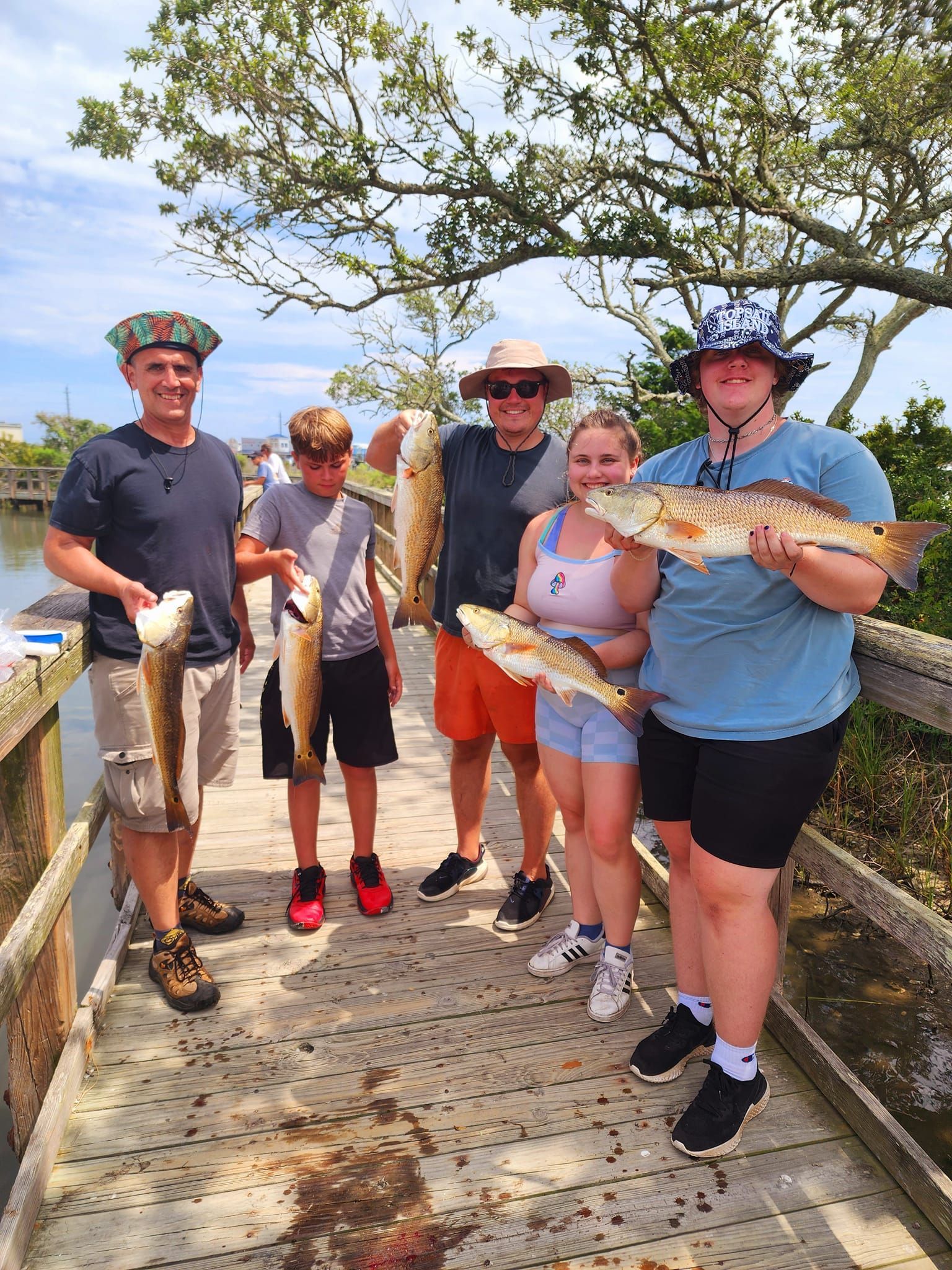 Five people holding fish on a wooden dock. Sunny day, clear sky.