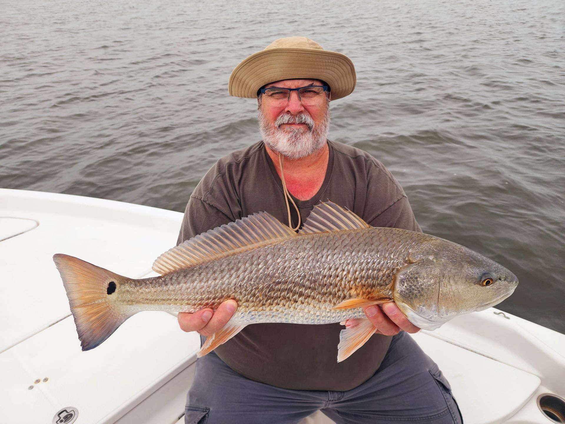 Man on boat holding a redfish; cloudy sky and water in the background.