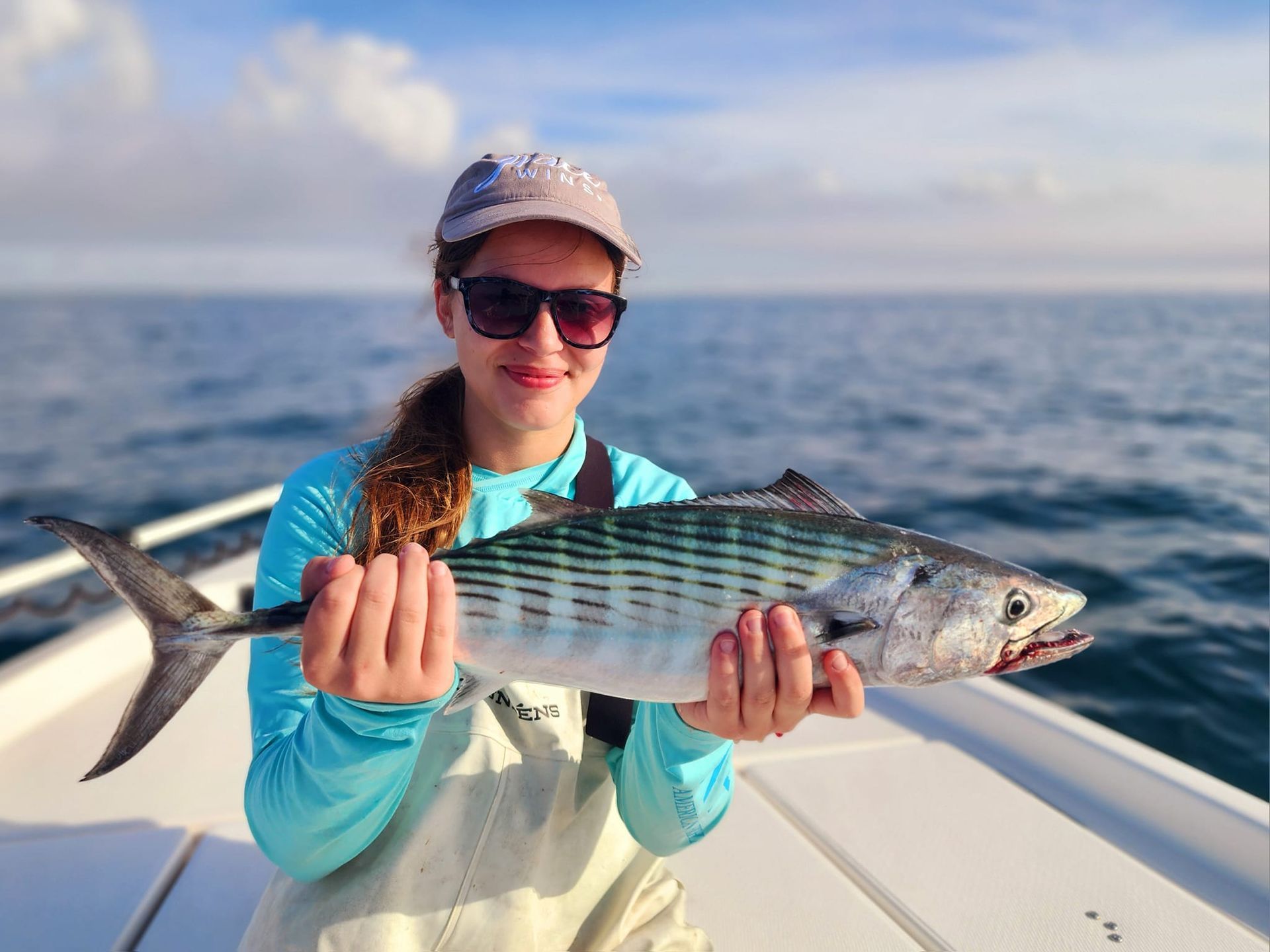 Woman holding a fish on a boat; blue ocean and sky in background.