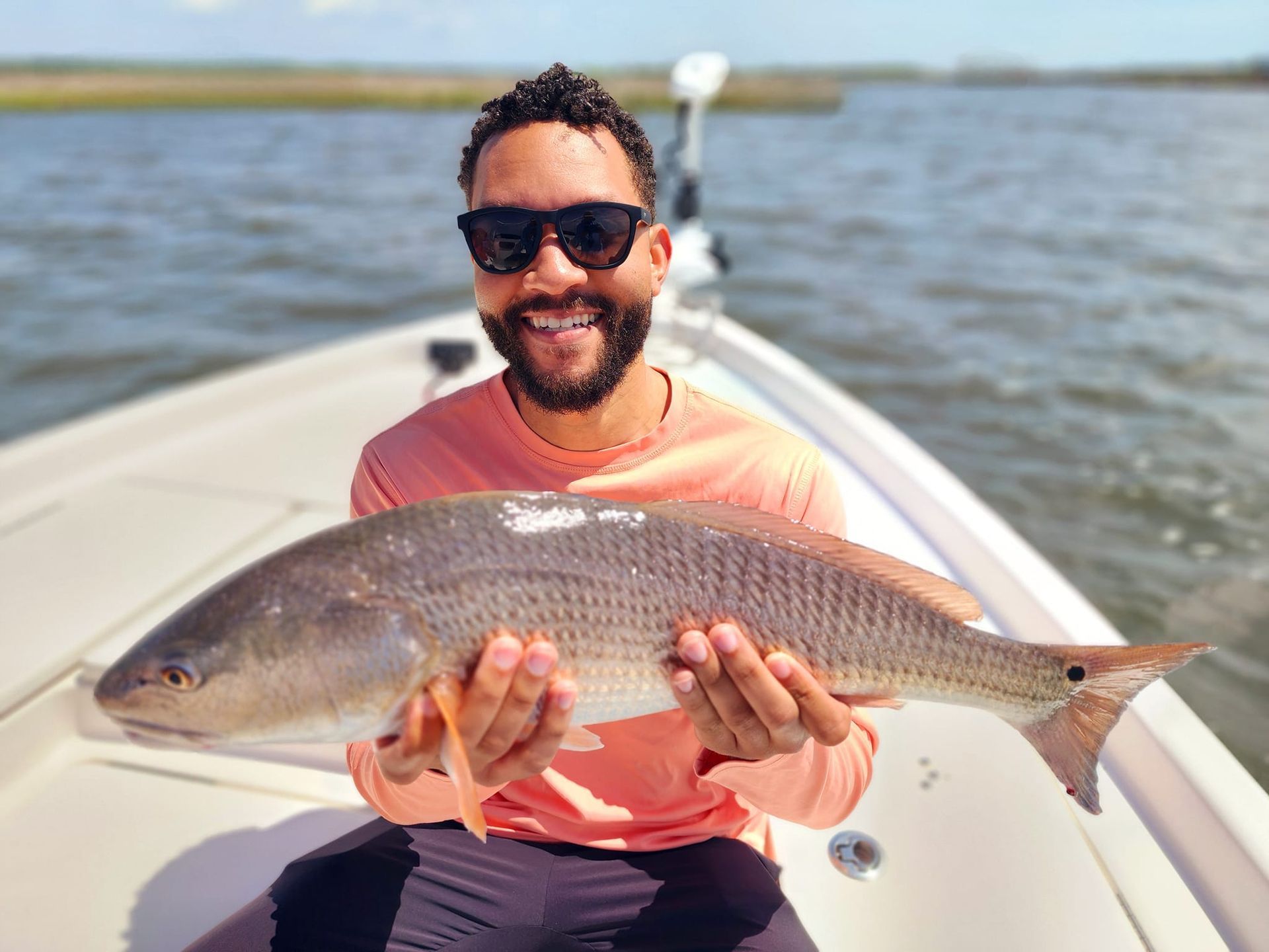 Man on boat holding a large redfish. Smiling, sunglasses, sunny day.
