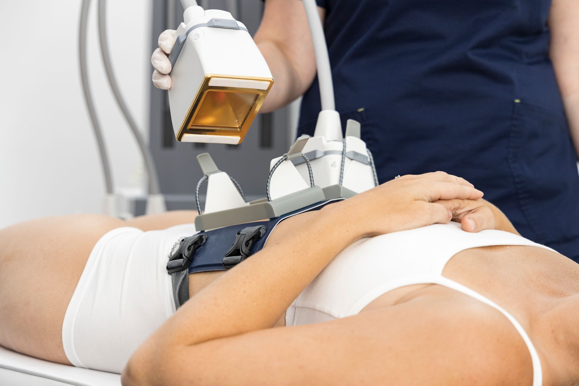 Laser treatment on a patient lying on a clinic bed, with a clinician holding the device over the abdomen.