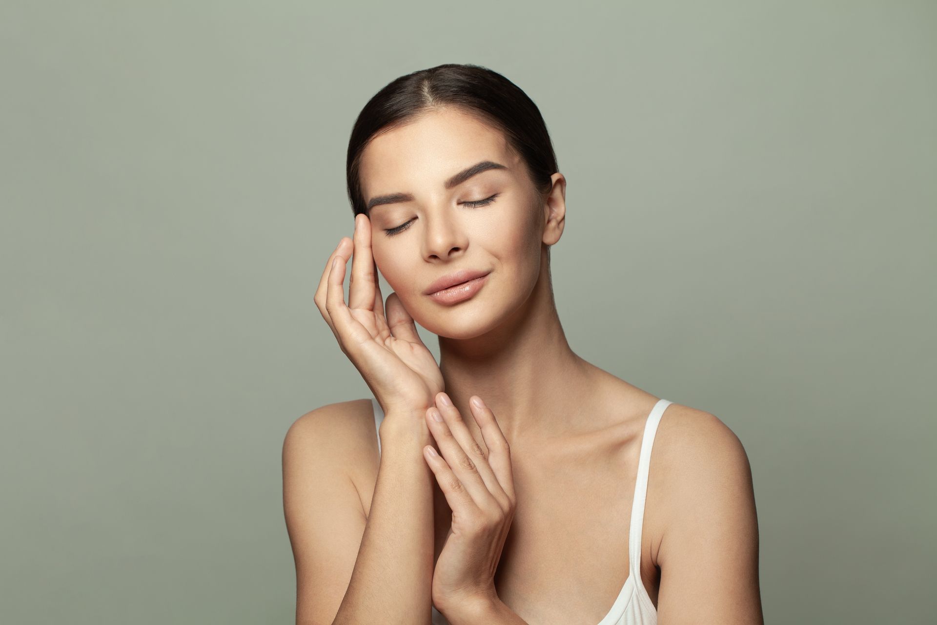 A woman is touching her face with her hands and smiling.