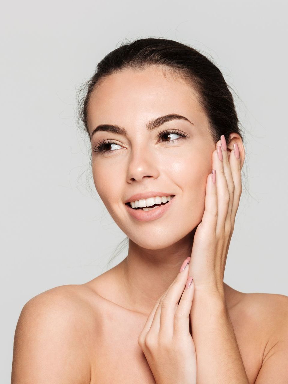 A woman is touching her face with her hands and smiling.