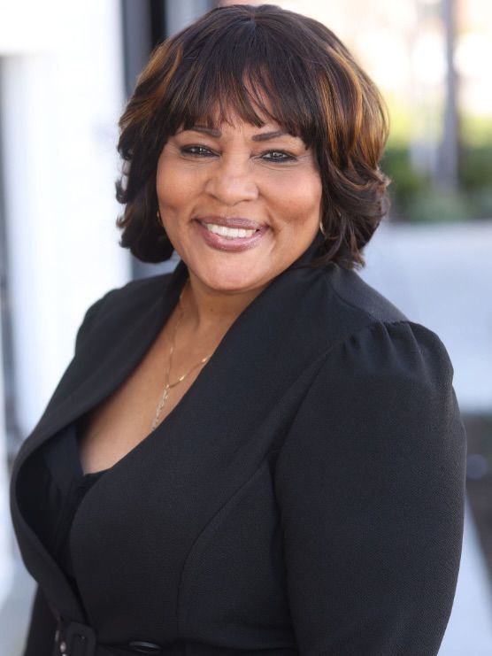 Smiling woman in a black blazer with short brown hair, posing against a softly blurred background