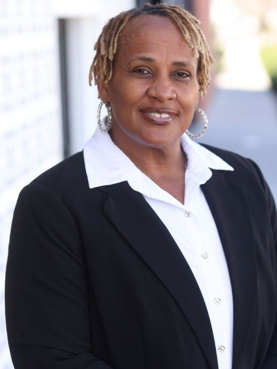 Portrait of a smiling person in a black blazer and white shirt against a bright blurred background