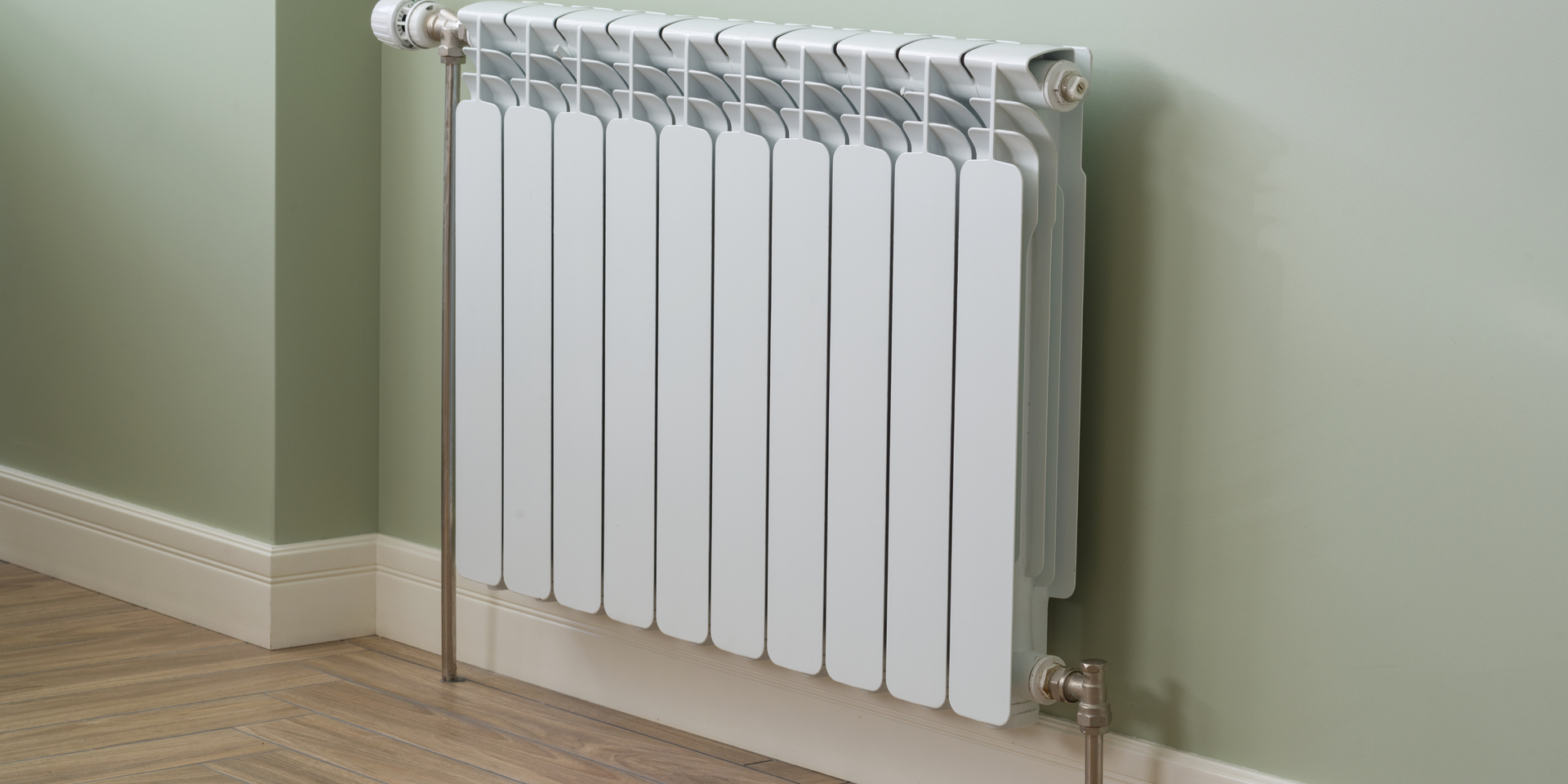 A white sectional radiator mounted on a light green wall above a wood-look floor.