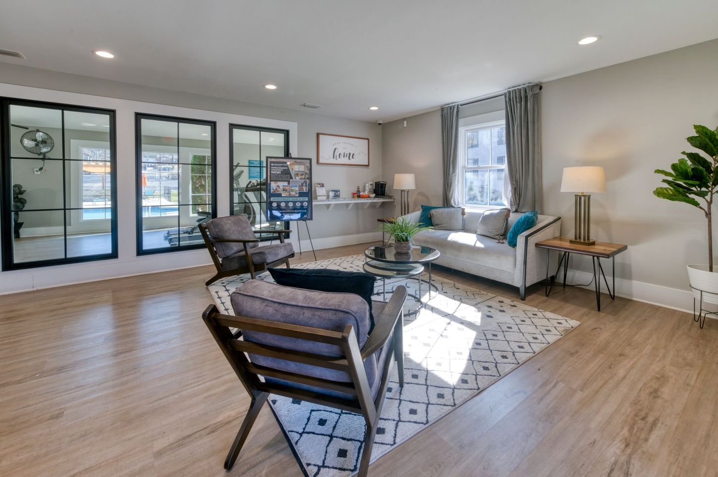 Bright open living room with gray sofa, armchairs, patterned rug, and large windows letting in daylight.