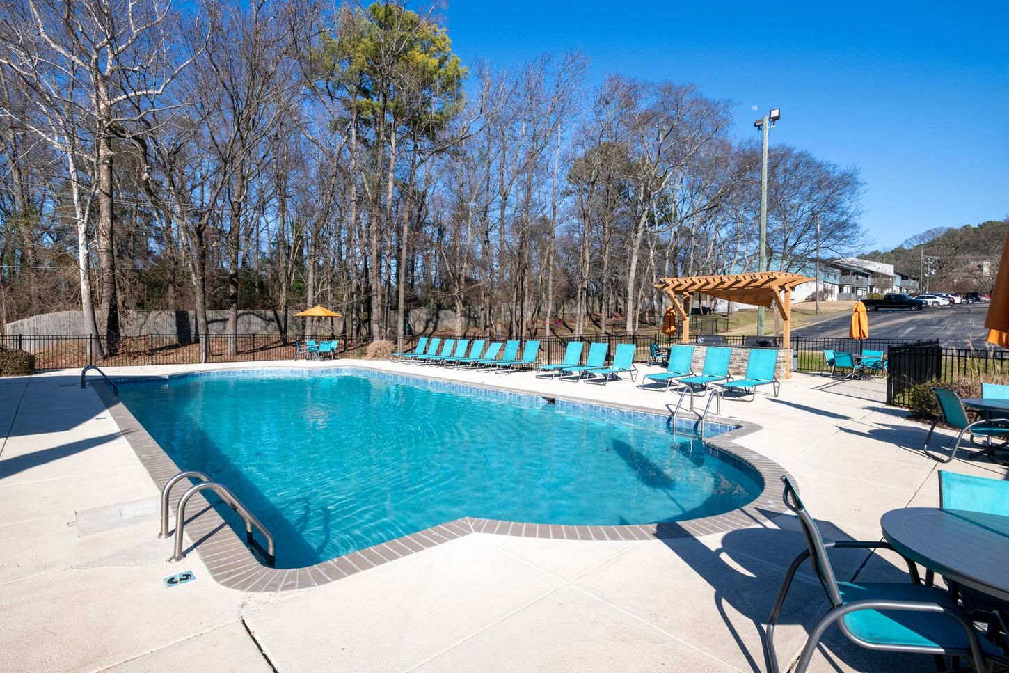Outdoor swimming pool with turquoise water, lounge chairs, and trees under a clear blue sky