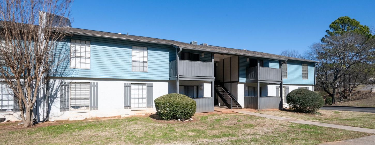 Two-story apartment building with light blue siding and white trim on a sunny day