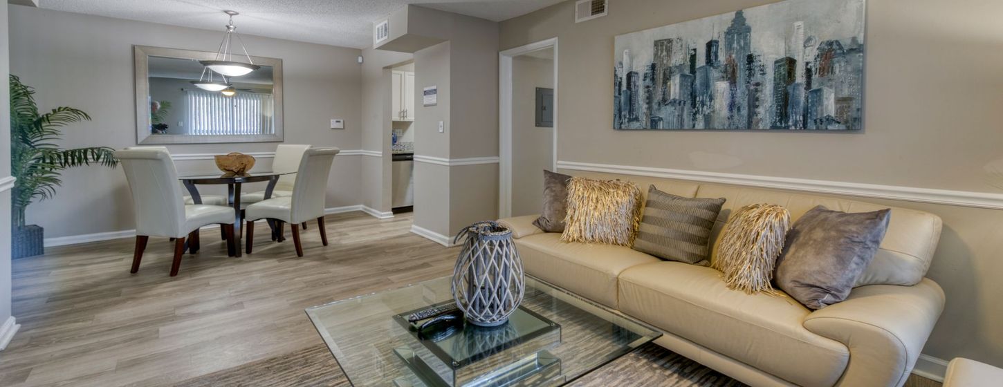 Modern living room with beige sectional, glass coffee table, and dining area by a kitchen pass-through