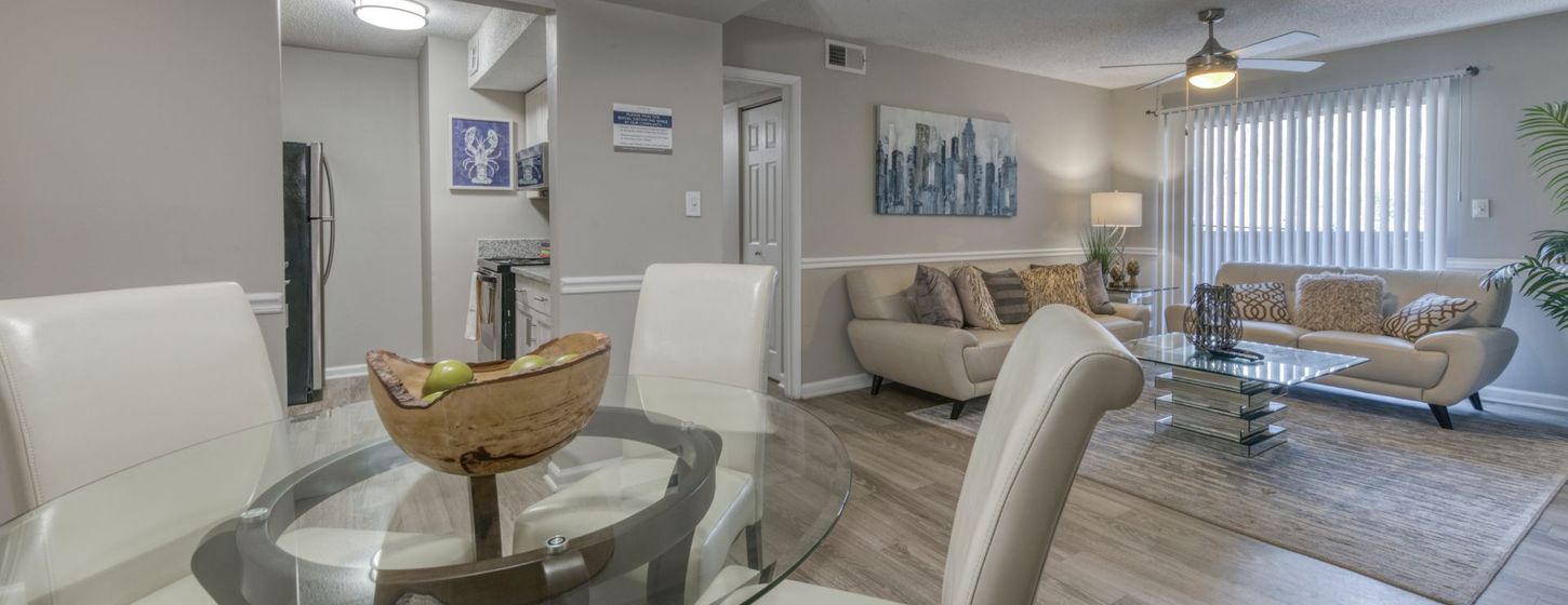 Bright open dining and living room with white chairs, glass table, sofa, fan, and sheer curtains