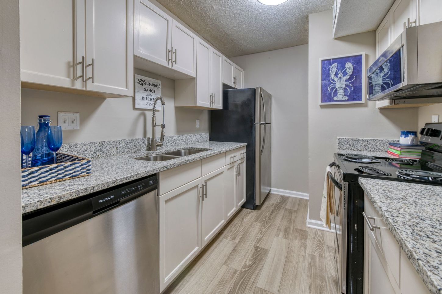 Bright modern kitchen with granite counters, white cabinets, stainless appliances, and light wood floors