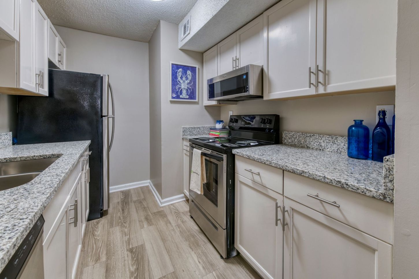 Modern kitchen with white cabinets, granite counters, stainless steel appliances, and light wood flooring