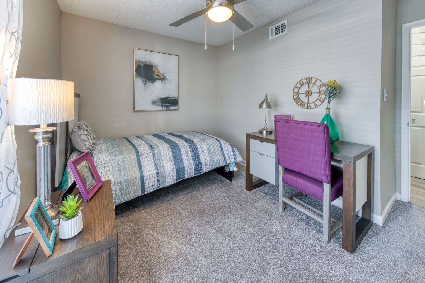 Small bedroom with twin bed, desk, purple chair, floor lamp, and ceiling fan.