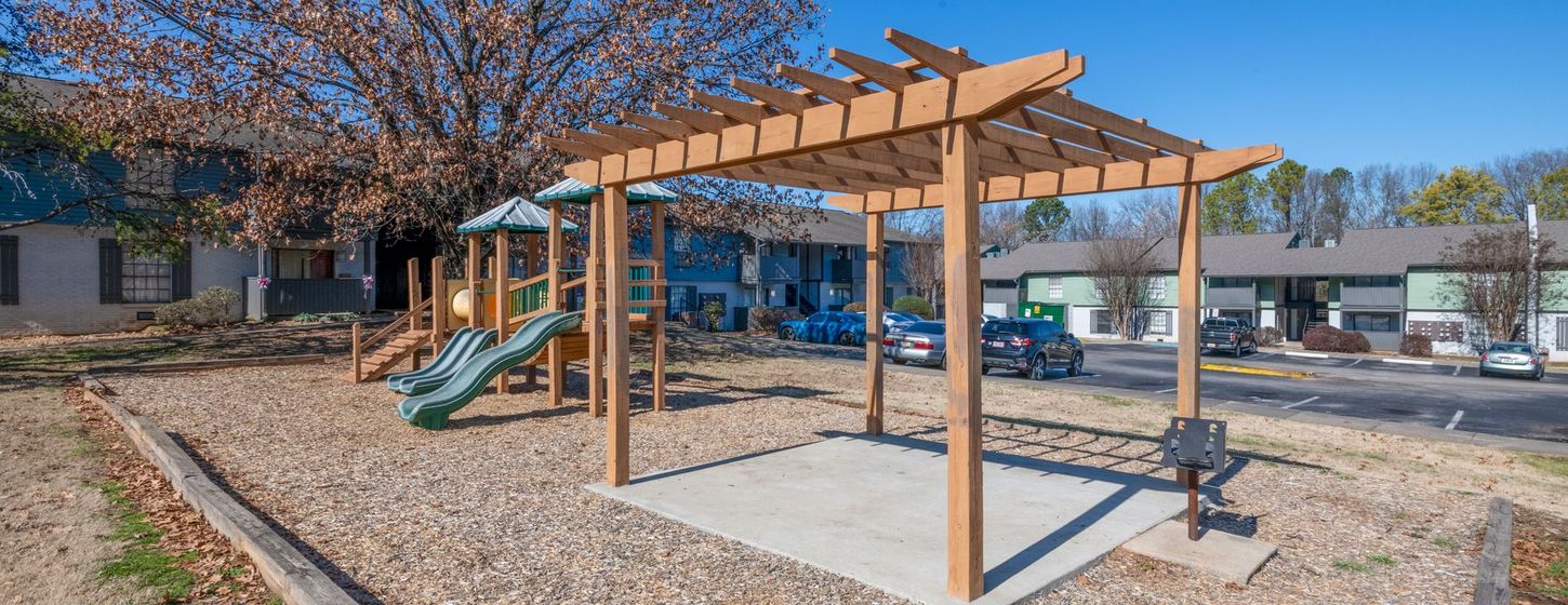 Playground with wooden pergola, swings, slide, and benches in a sunny park
