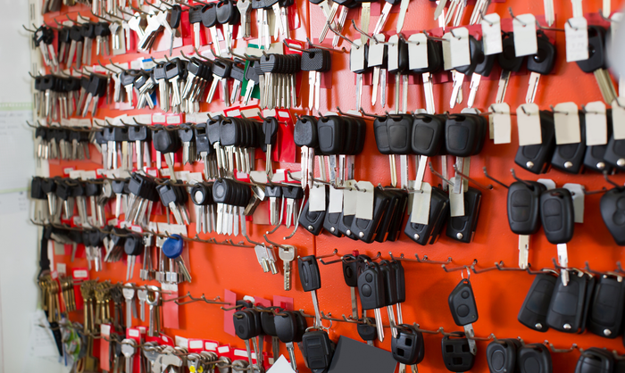 Wall of keys and key fobs for sale, orange background.