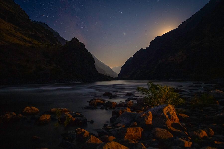 River flowing through a canyon at night with the moon shining through the mountains