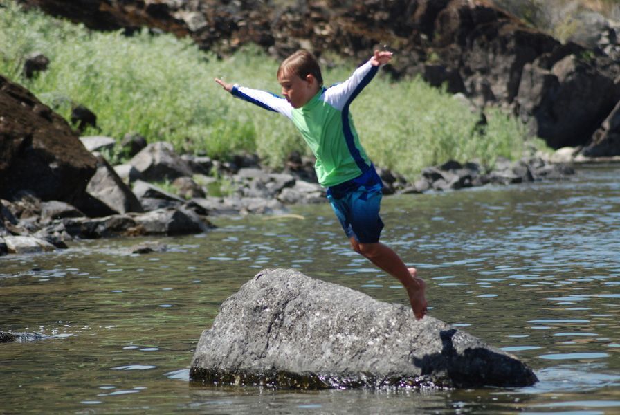 Young Boy Is Jumping Off a Rock Into a River