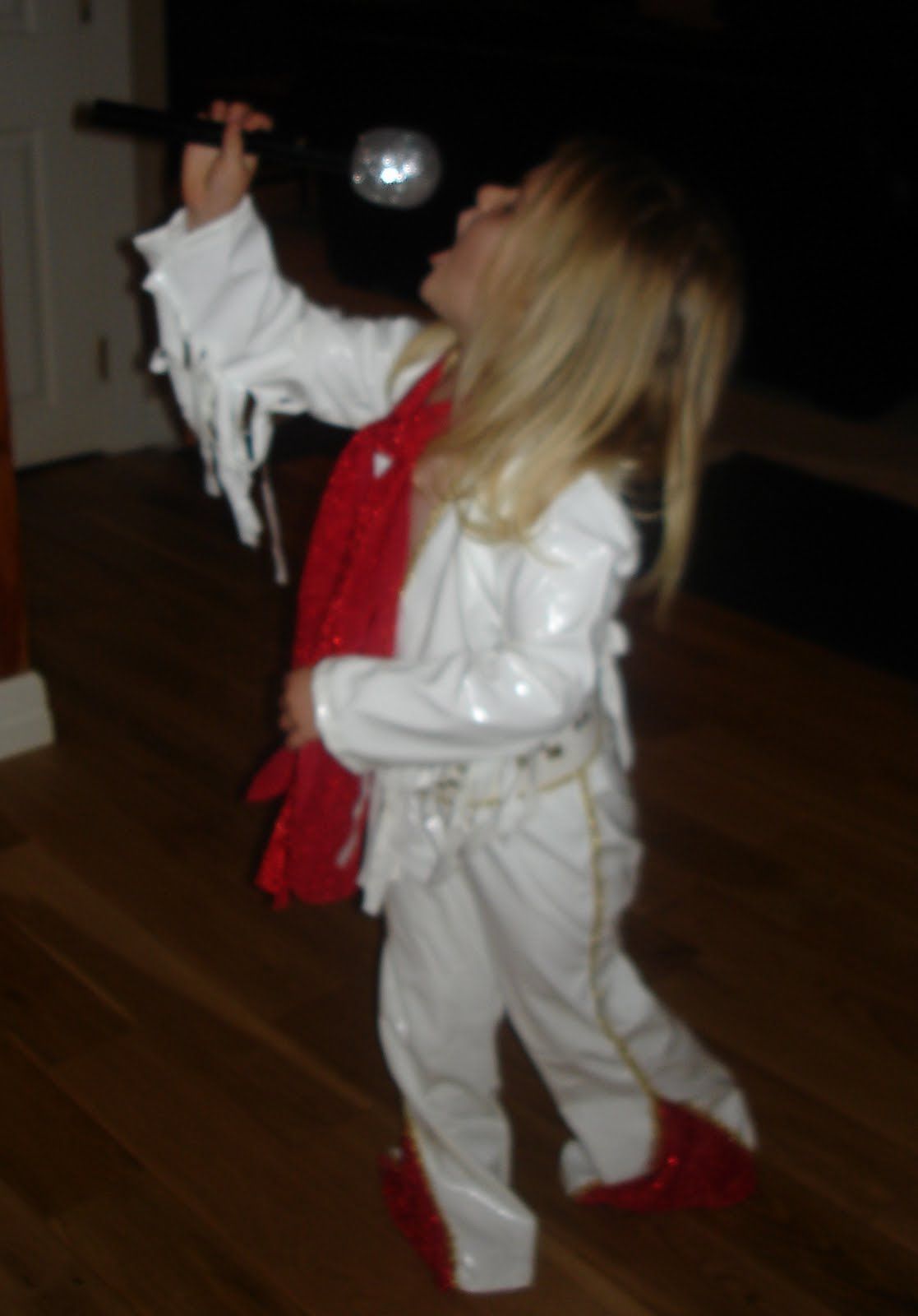 A little girl in a white outfit is singing into a microphone
