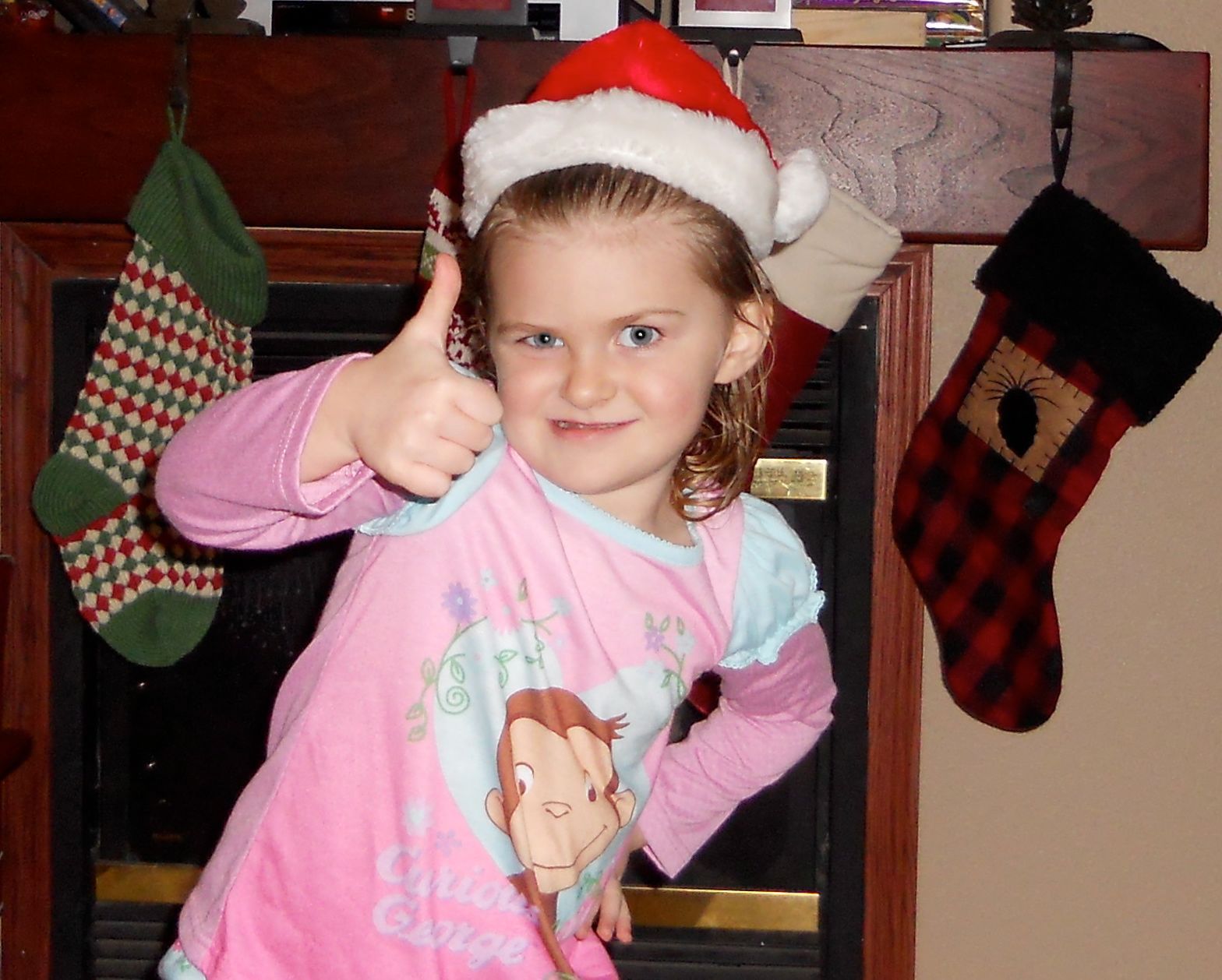 A little girl wearing a santa hat gives a thumbs up