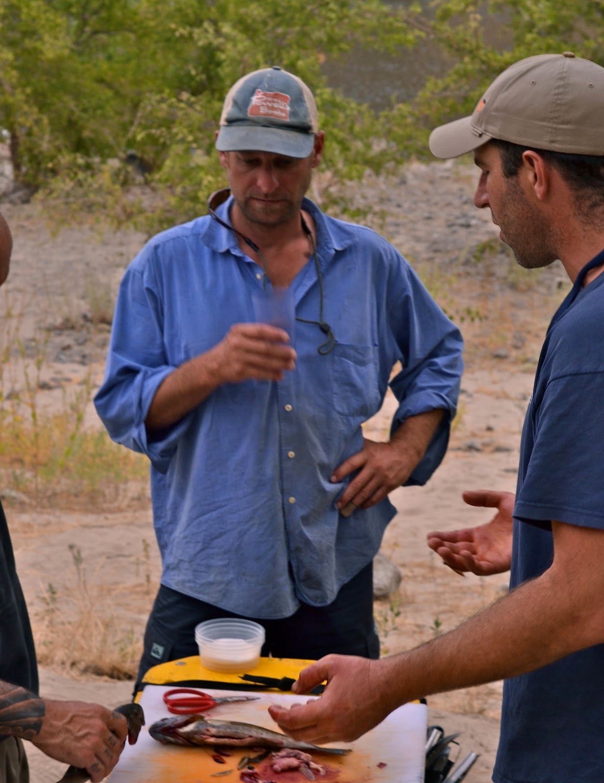 Three men are standing around a table with a fish on it