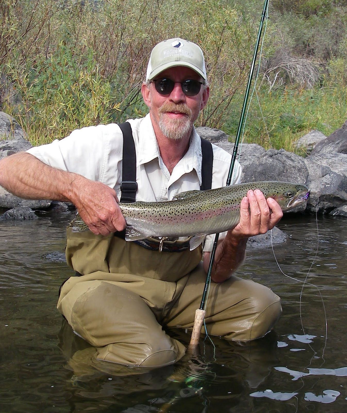 A man is kneeling in the water holding a rainbow trout