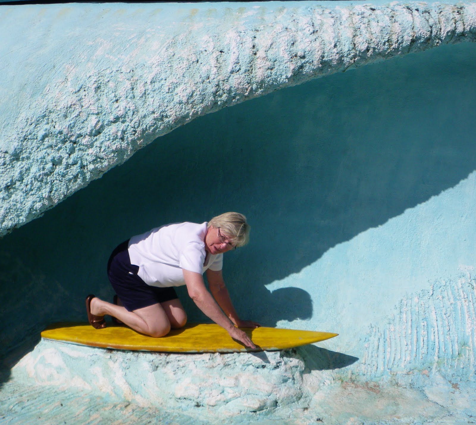 A woman is kneeling on a yellow surfboard in front of a blue wall