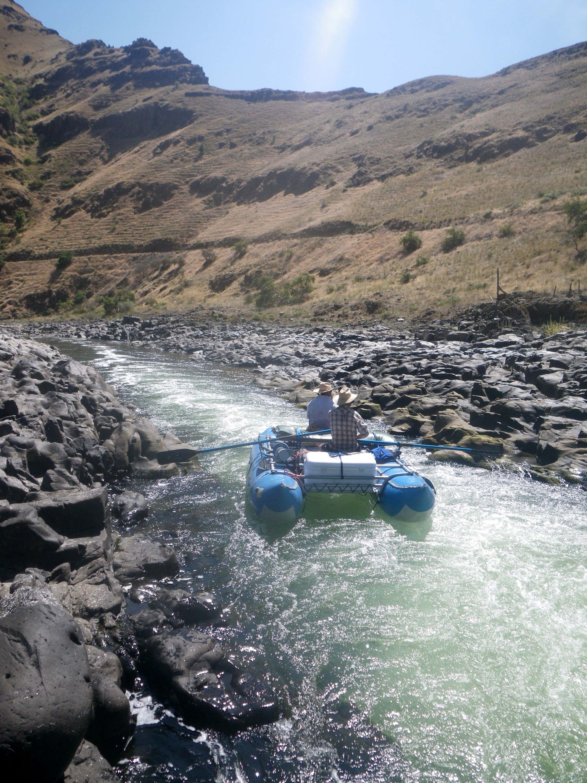 Two people in a raft in a river with mountains in the background