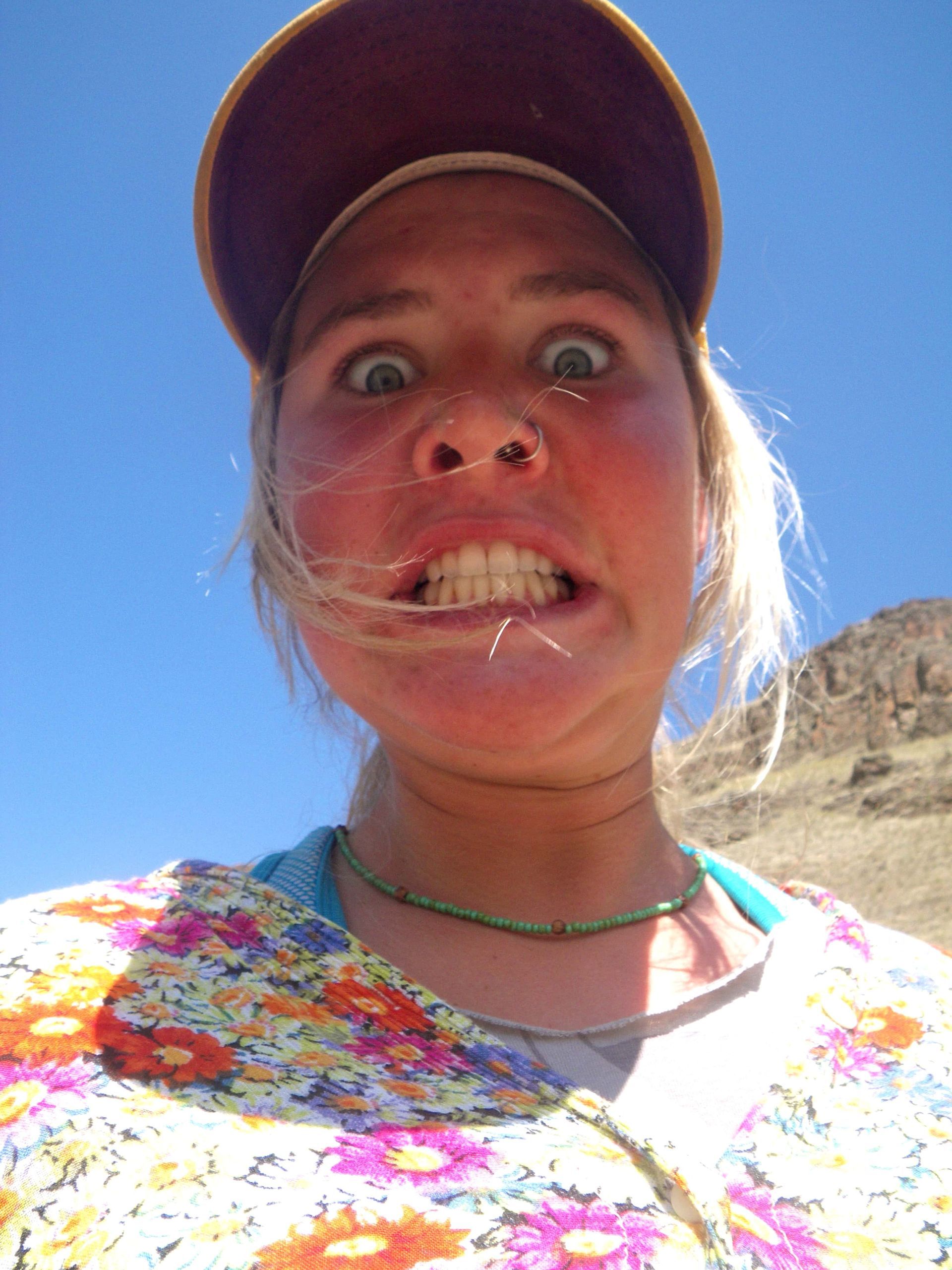 A woman wearing a hat and a floral shirt is making a funny face