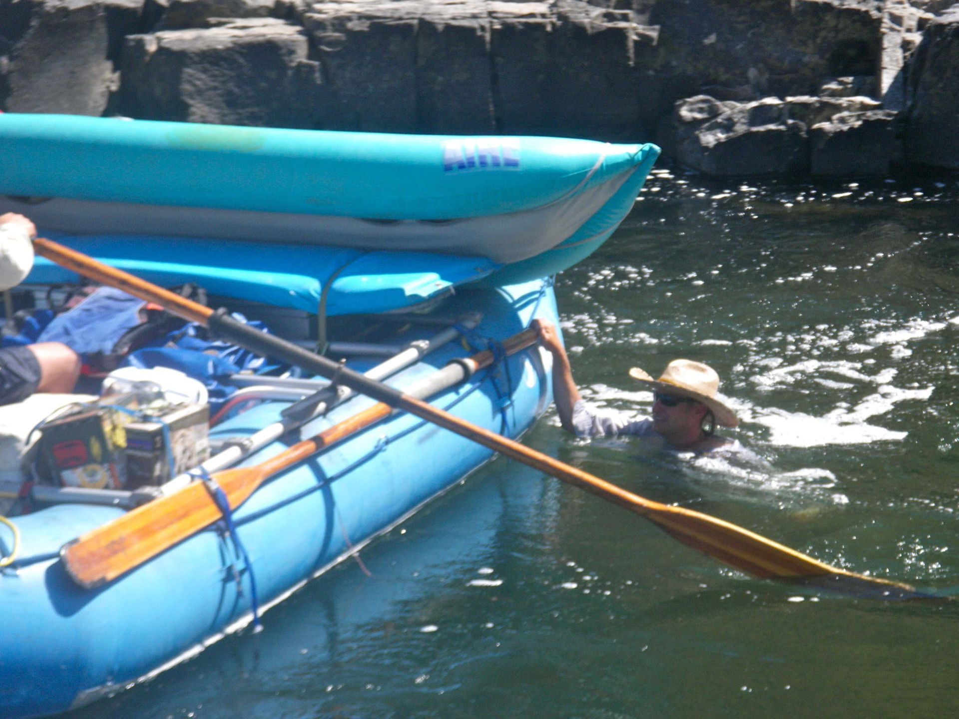 A man in a cowboy hat is paddling a blue raft