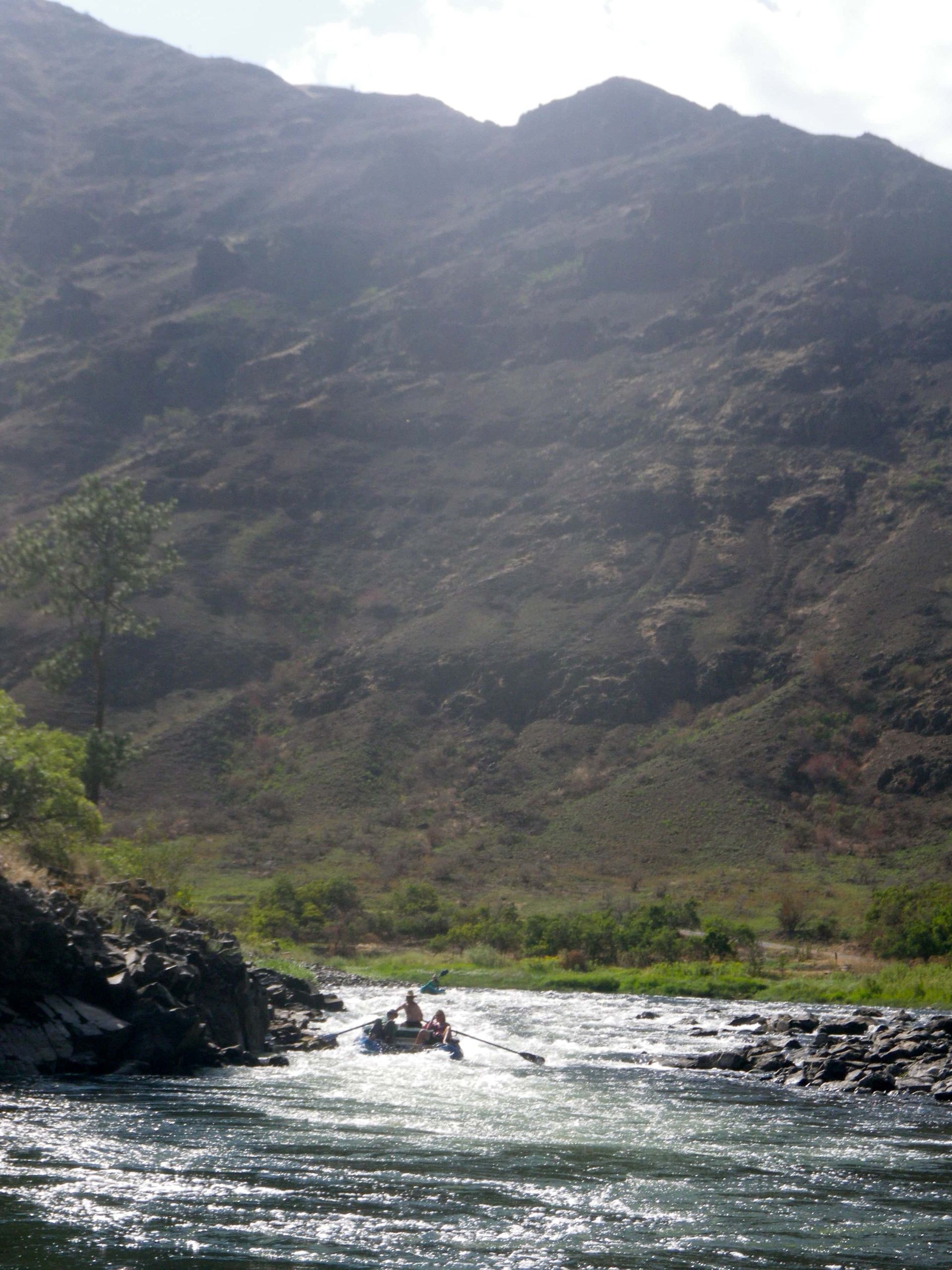A river with mountains in the background and people in a raft