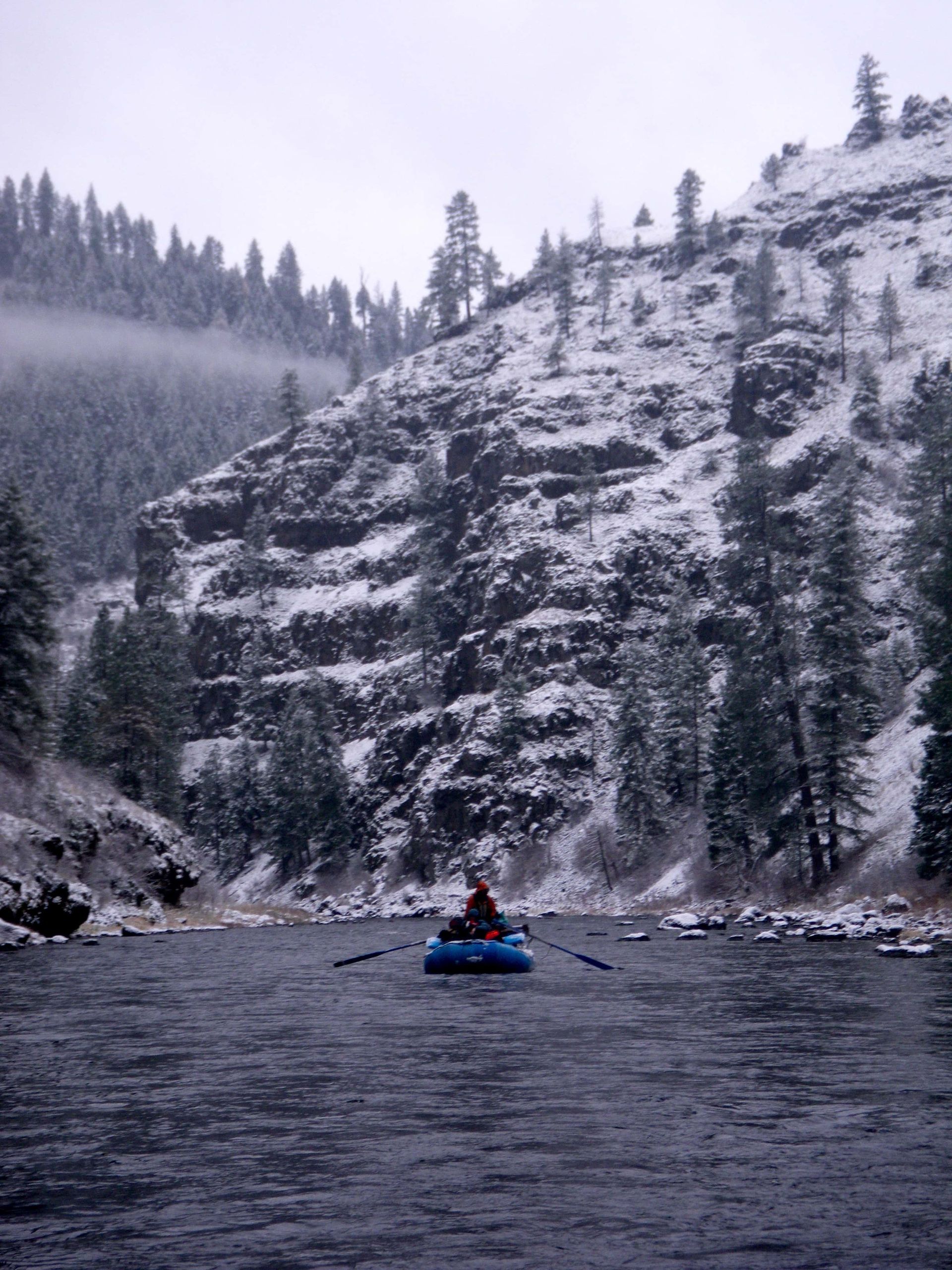 A man in a blue raft is paddling down a river.