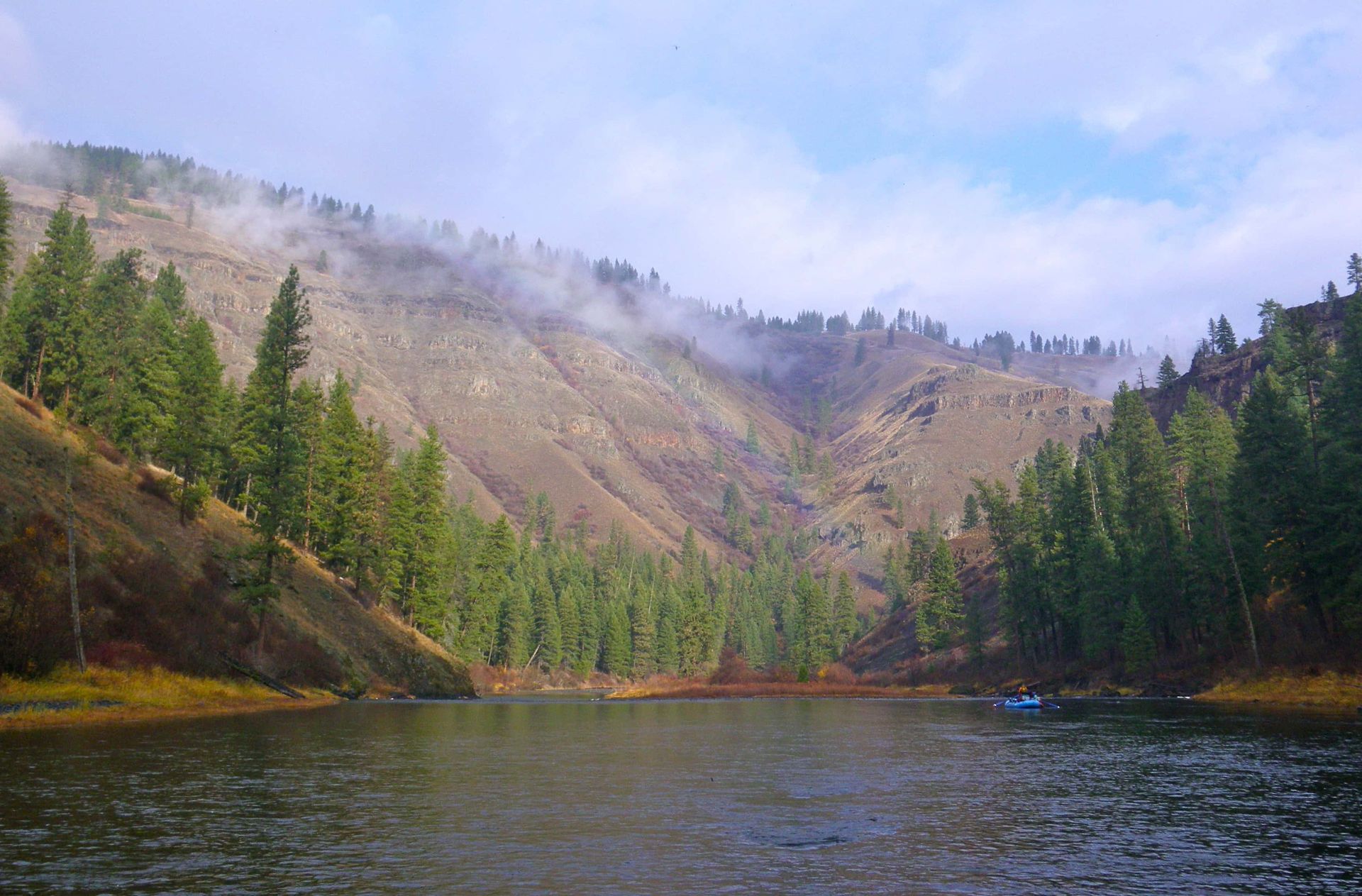A lake surrounded by mountains and trees on a cloudy day