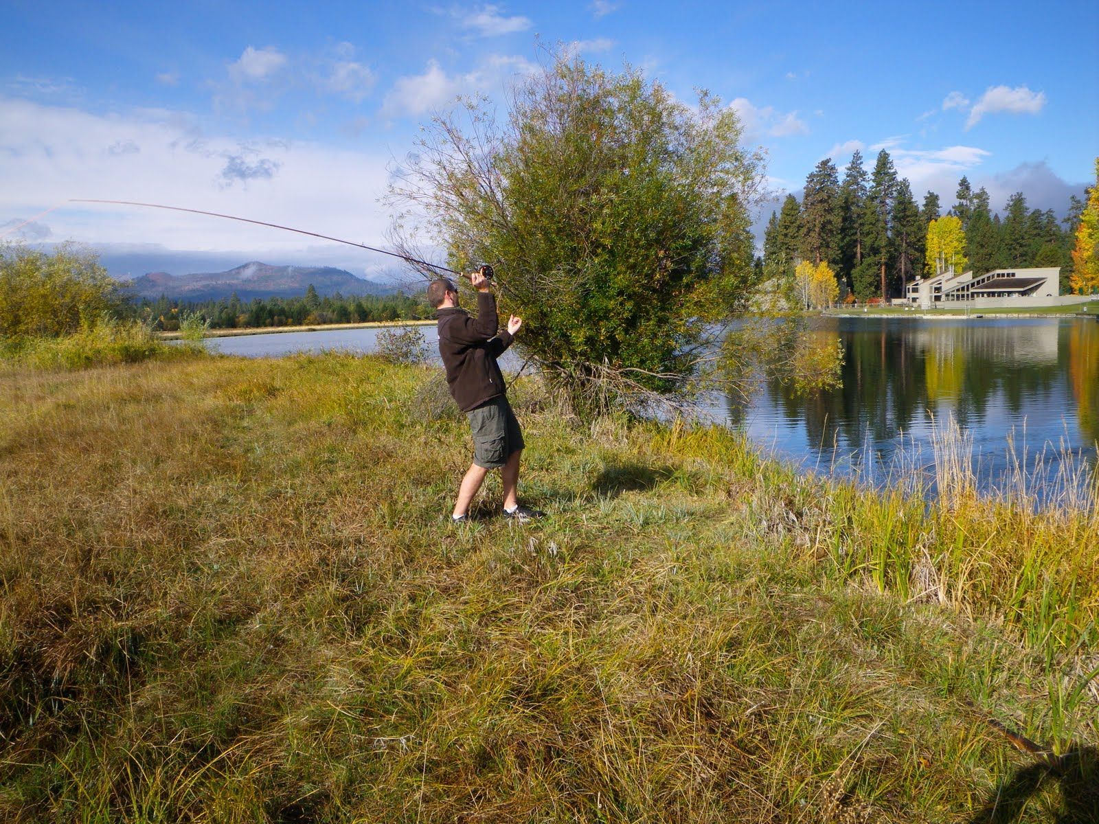 A man is fishing in a field next to a lake.