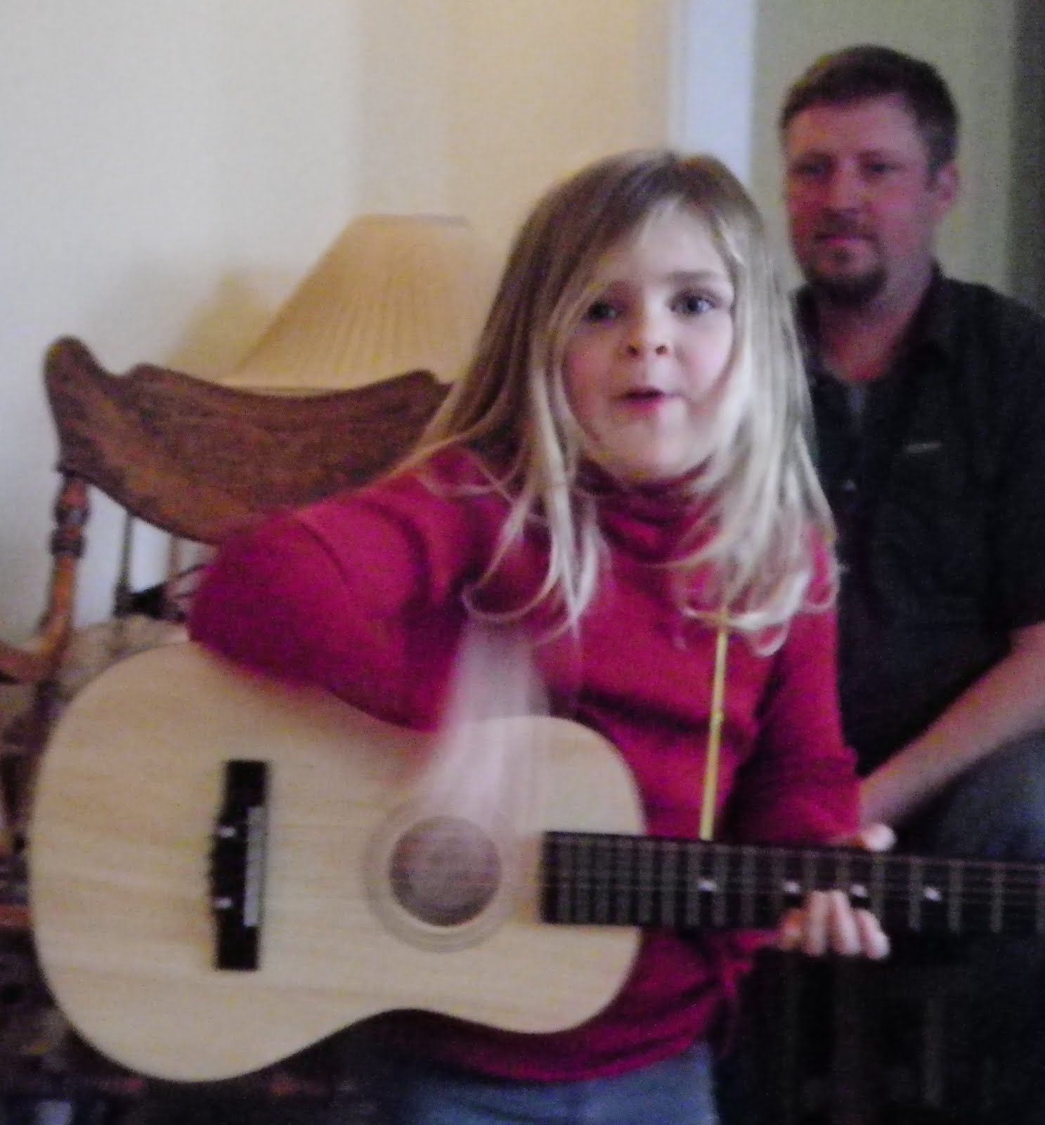 A little girl in a red sweater is holding a guitar