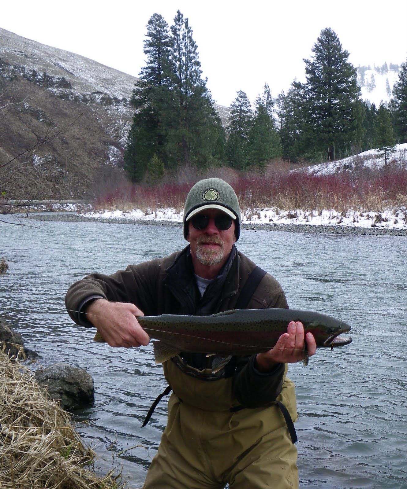 A man is holding a large fish in front of a river