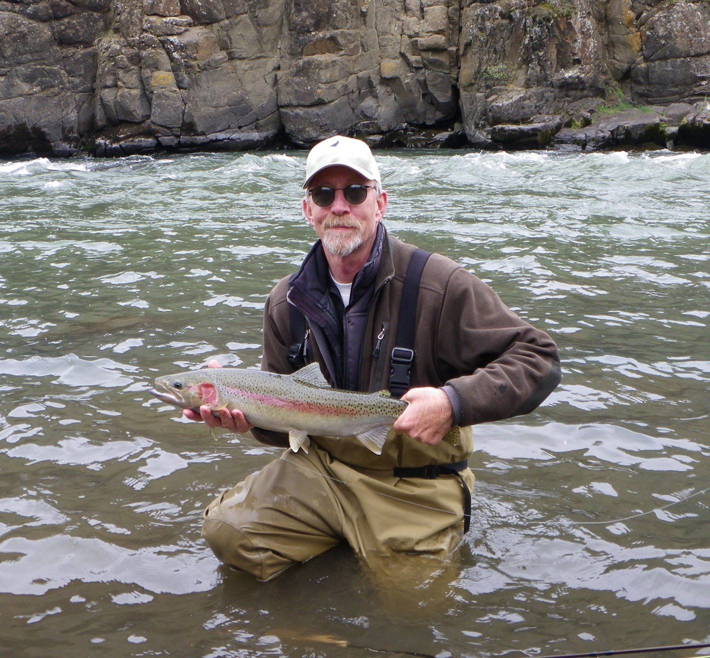 A man is kneeling in the water holding a fish