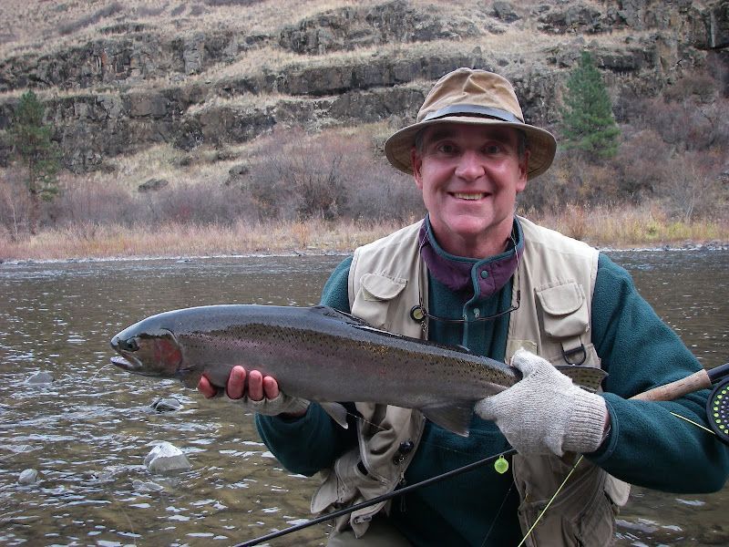 A man in a hat is holding a large fish in front of a river.