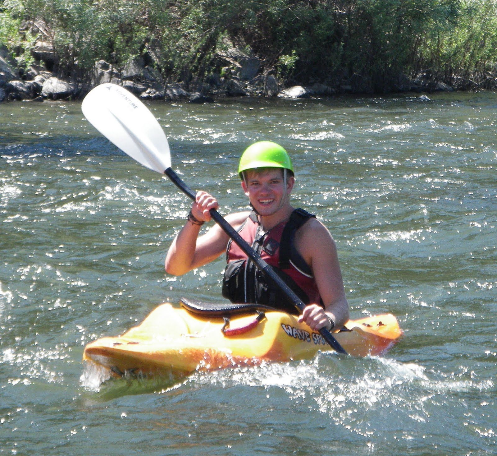 A man wearing a green helmet is paddling a yellow kayak