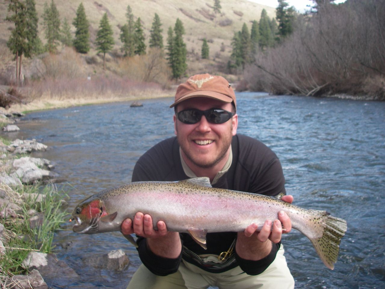 A man is holding a rainbow trout in front of a river