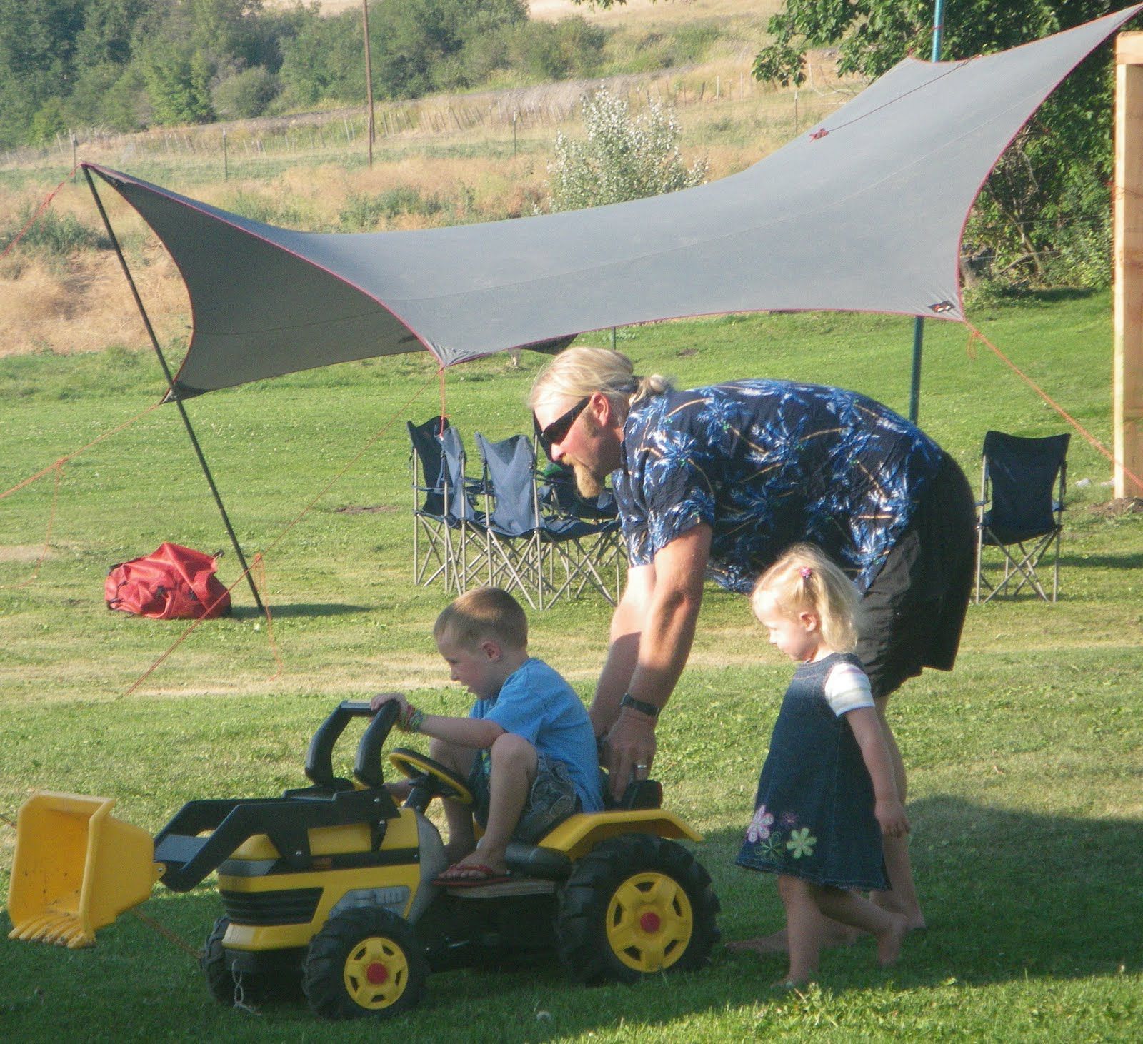 A man and two children are playing with a toy tractor