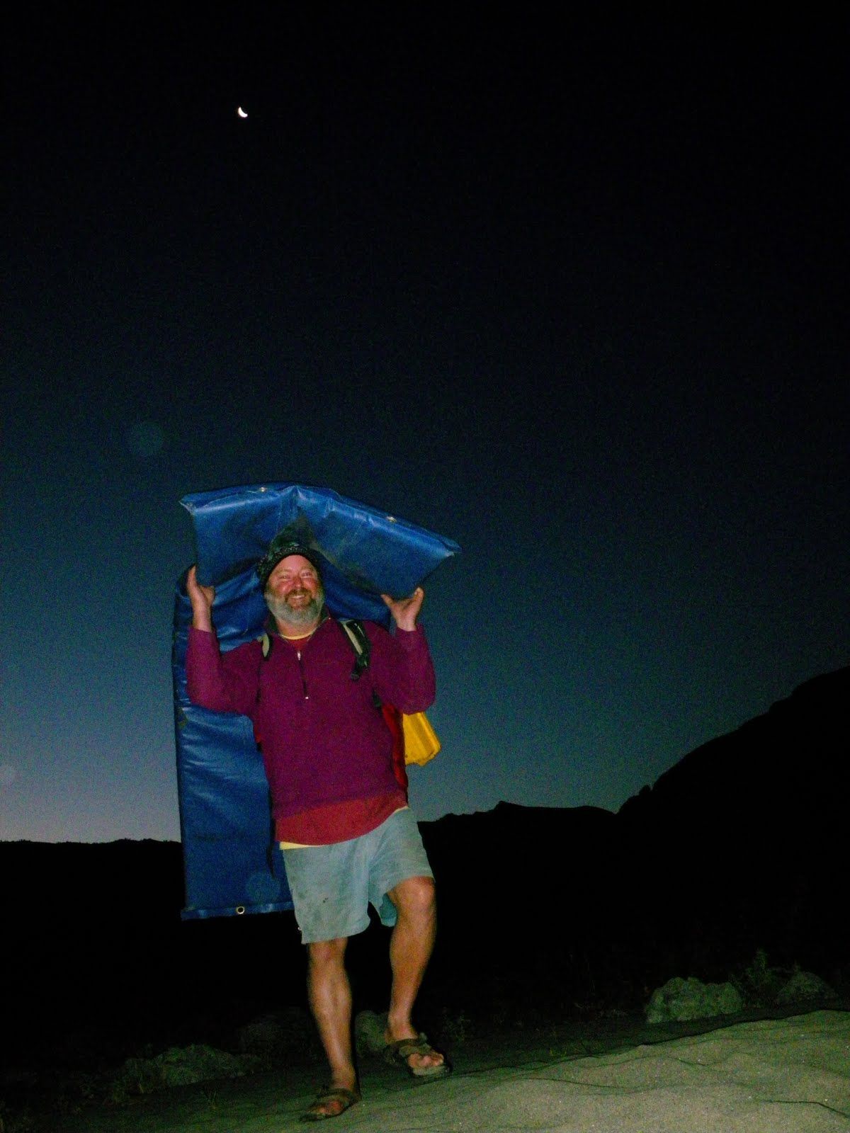 A man in a purple shirt is carrying a blue bag on his shoulders