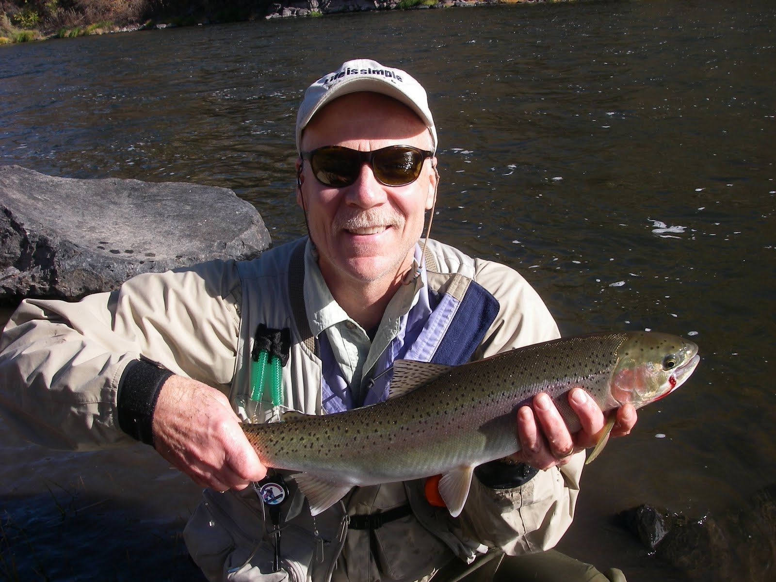 A man holding a rainbow trout in front of a river